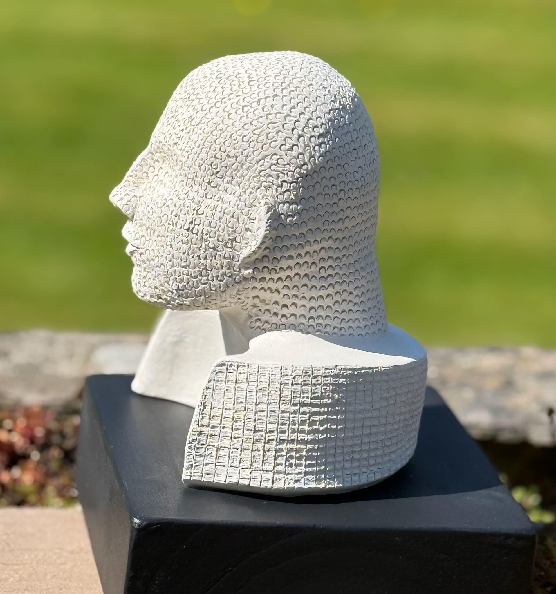 White ceramic head bust with stippled, chain-mail-like texture, frontal view