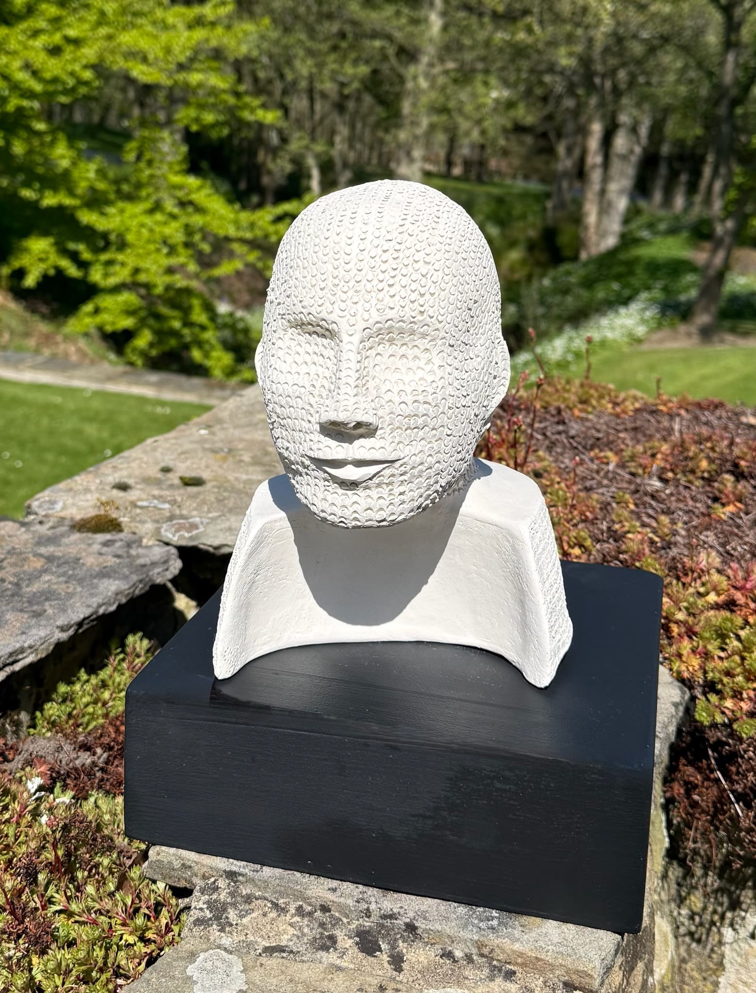White ceramic head bust with stippled, chain-mail-like texture, profile view