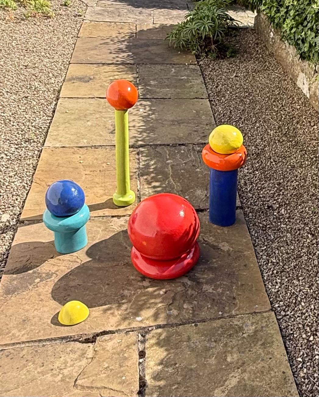 Brightly glazed ceramic forms arranged on a stone pathway beside a wall