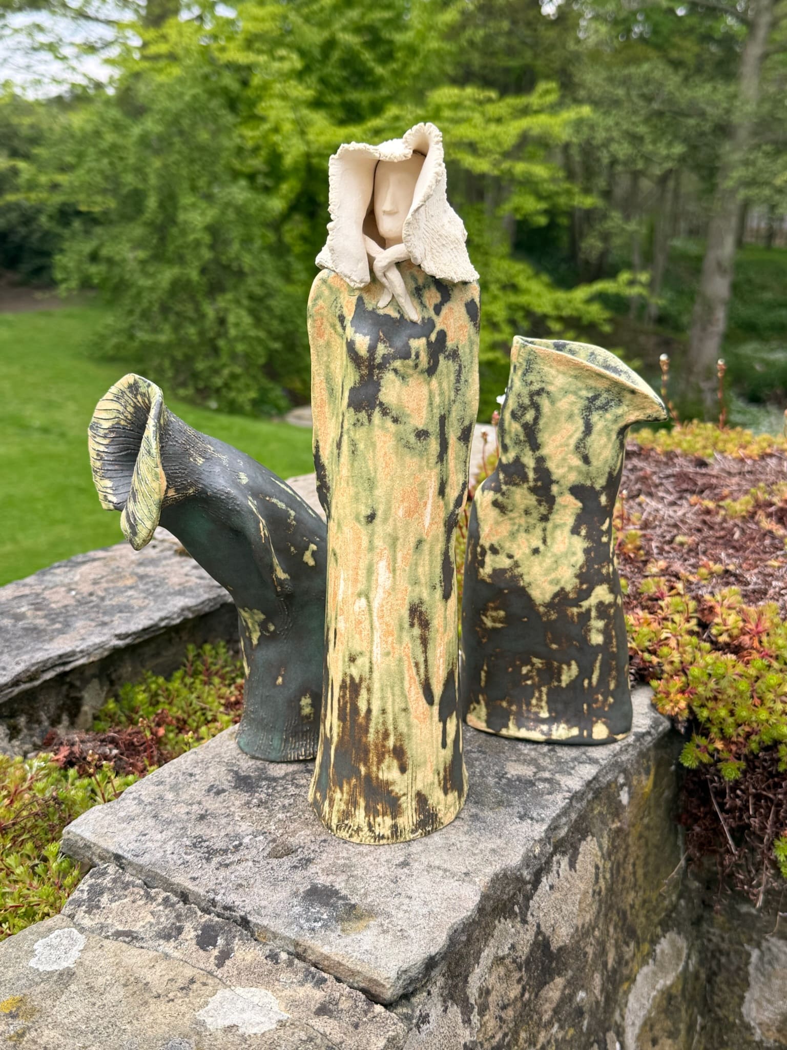 Three hooded ceramic figures grouped on a garden wall