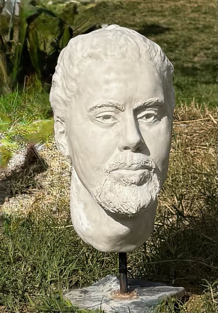 White ceramic portrait head of a bearded man on a stand in a garden